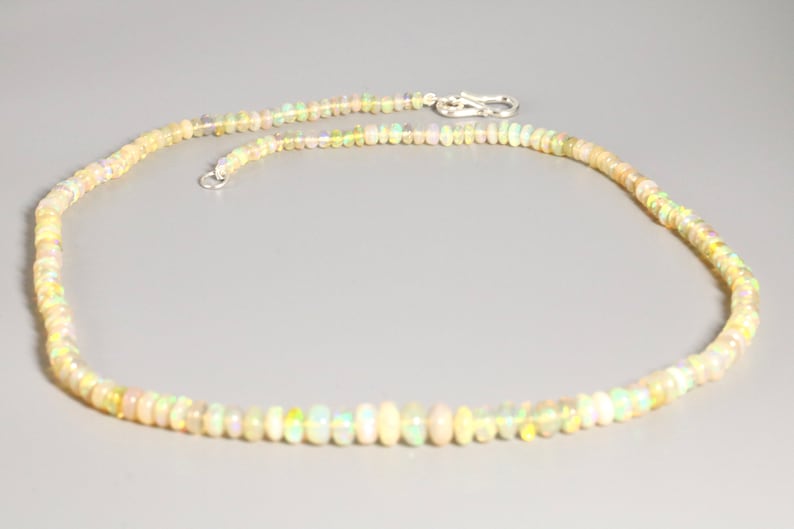 May include: A delicate necklace made of small, iridescent opal beads. The necklace is strung on a silver chain and has a silver clasp.