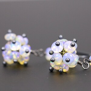 May include: A pair of silver earrings with clusters of iridescent white opal beads and small black beads.