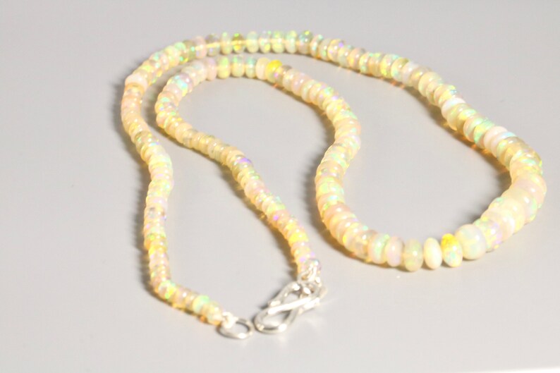 May include: A white opal beaded necklace with a silver clasp. The necklace is made of small, round beads that are strung together on a silver chain.