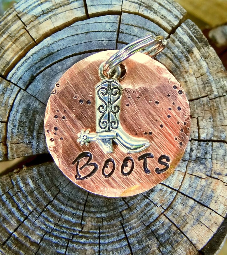 May include: A copper-colored round dog tag with a silver boot charm and the word "BOOTS" engraved on it.