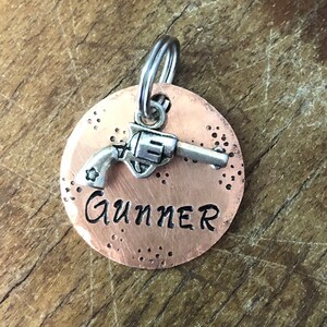 May include: Copper dog tag with a silver gun charm and the name "Gunner" engraved on it.