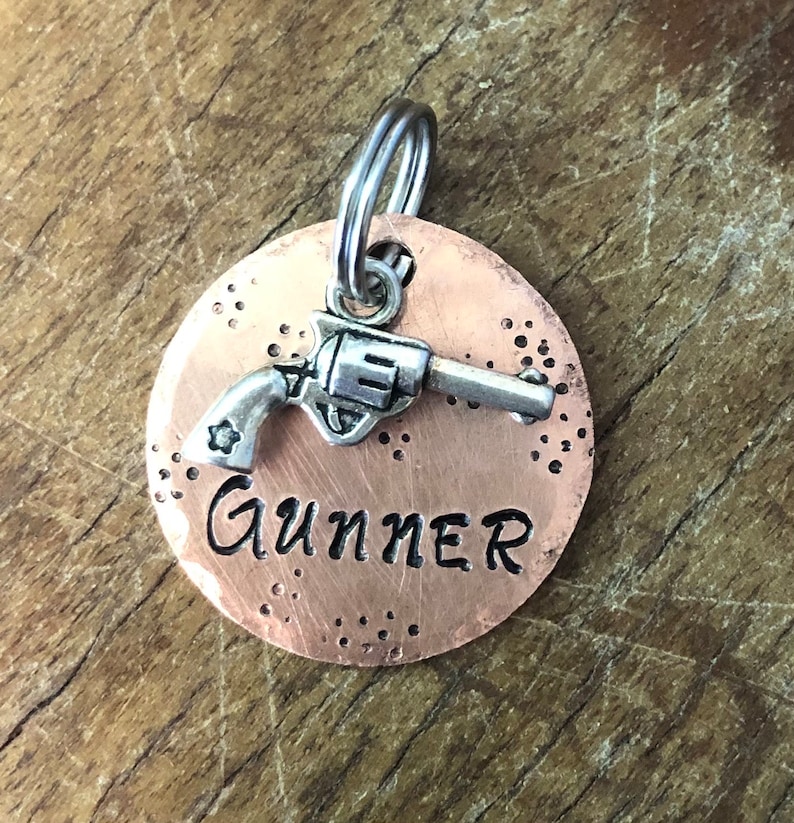 May include: Copper dog tag with a silver gun charm and the name "Gunner" engraved on it.