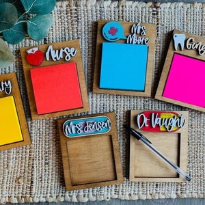 May include: Six wooden notepads with different designs and names. The notepads have a heart, a tooth, a speech bubble, and a first aid kit. The names on the notepads are "Mary", "Nurse", "Mrs. Moore", "Ginger", "Mrs. Jensen", and "Dr. Vaught".