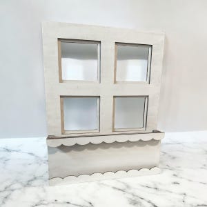 May include: A wooden dollhouse window with four square window panes. The window has a scalloped flower box attached to the bottom. The window is painted in a light, neutral color.