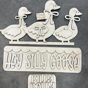 May include: Wooden cutouts of three geese with bow ties, a sign that says "Honk Honk", and a sign that says "Hey Silly Goose". A smaller sign says "Dilly Dally".