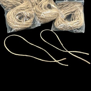 May include: Three bundles of natural twine in clear plastic bags, with two loops of twine in the foreground. The twine is a light brown color against a black background. The twine is likely used for crafting or packaging.