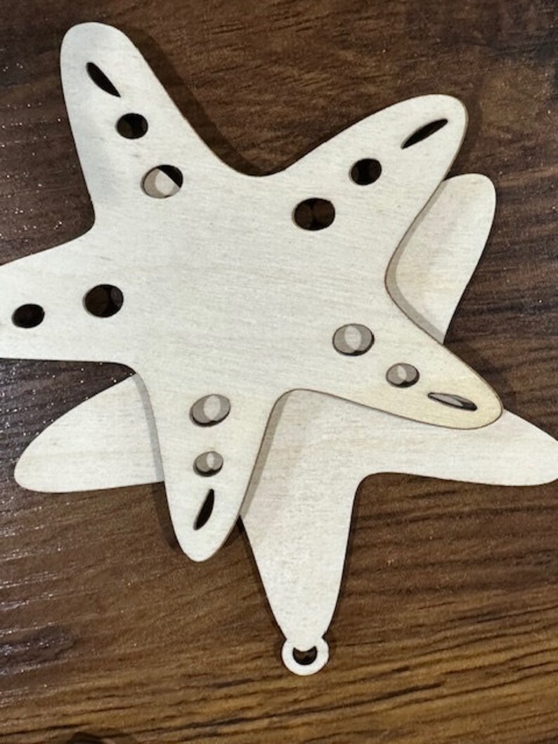 May include: A wooden cutout of a starfish with a hole in the center for hanging. The starfish is painted white and has a natural wood grain.