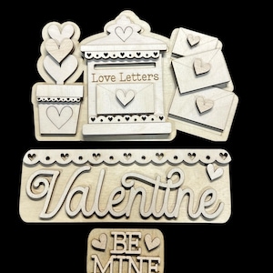 May include: Wooden Valentine's Day craft kit with a mailbox, envelopes, a flower pot, and a sign that says "Love Letters". There is also a sign that says "Valentine" and a smaller sign that says "Be Mine".