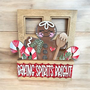 May include: A wooden Christmas door hanger with a gingerbread person, candy canes, and a wooden spoon. The sign reads "Baking Spirits Bright".