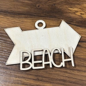 May include: Wooden arrow sign with the word "Beach" in white lettering. The sign is unfinished and ready to be painted or stained.
