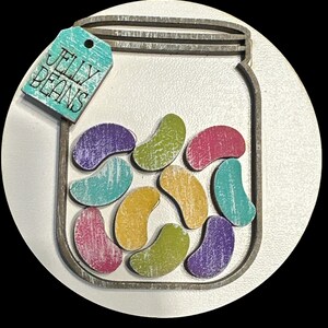 May include: A wooden cutout of a mason jar filled with colorful jelly beans. The jar has a tag that says "Jelly Beans".