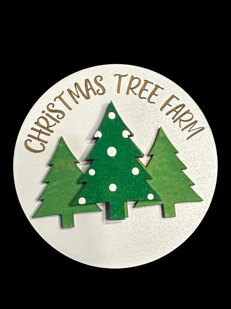 May include: A white round wooden sign with the text "Christmas Tree Farm" in gold lettering. Three green Christmas trees with white polka dots are layered on top of the text.