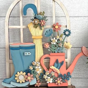 May include: A wooden decorative piece featuring a light blue rain boot, a yellow sheaf of wheat, and a coral watering can. The scene is adorned with colorful paper flowers and a blue bird, set against a white window frame.