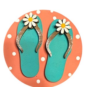 May include: A pair of turquoise blue flip flops with white daisy flowers on the straps, on a coral pink background with white polka dots.