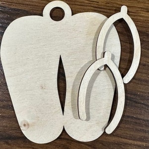 May include: Wooden cutout of a pair of flip flops with two smaller cutouts of flip flops inside. The cutouts are unfinished and ready to be painted or stained.