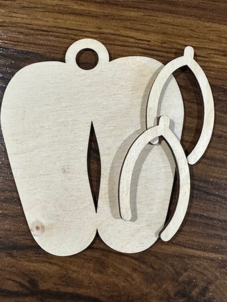 May include: Wooden cutout of a pair of flip flops with two smaller cutouts of flip flops inside. The cutouts are unfinished and ready to be painted or stained.