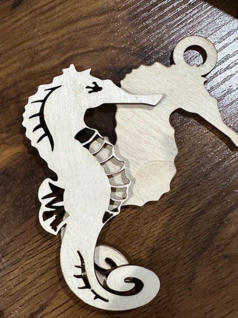 May include: A wooden cutout of a seahorse with a decorative swirl design. The seahorse is painted white and has black details.