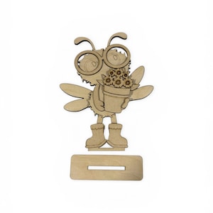 May include: Wooden cutout of a cartoon bee wearing glasses and boots, holding a flower pot. The bee has wings and antennae. The cutout is on a rectangular base with a slot.