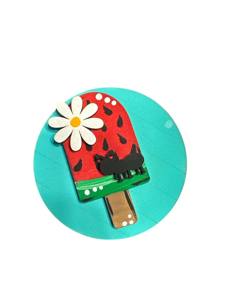 May include: A round wooden sign with a turquoise background features a watermelon popsicle with a white flower and a black ant. The popsicle is painted red with black seeds and a green stripe. The stick is brown with white dots.