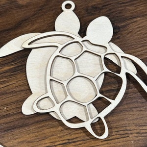 May include: A wooden cutout of two sea turtles, one on top of the other. The top turtle has a detailed shell design.
