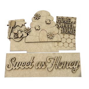 May include: A wooden decorative sign featuring a honey-themed design. The sign includes a honey jar, a beehive, and the phrase "Home Sweet Home." The bottom of the sign reads "Sweet as Honey."