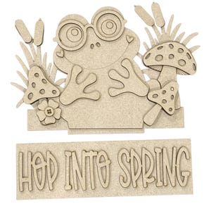 May include: A wooden frog wearing glasses, surrounded by mushrooms and cattails. The phrase "HOP INTO SPRING" is displayed below the frog. The design is made of light brown wood.