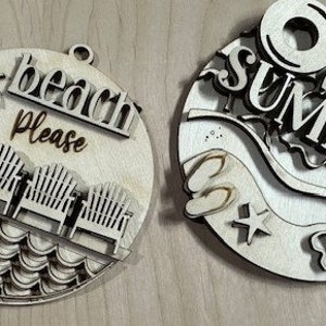 May include: Two round wooden ornaments with a summer theme. One ornament features a palm tree, beach chairs, and waves with the text "beach please". The other ornament features the text "hello summer" with a beach umbrella, flip flops, and a wave.
