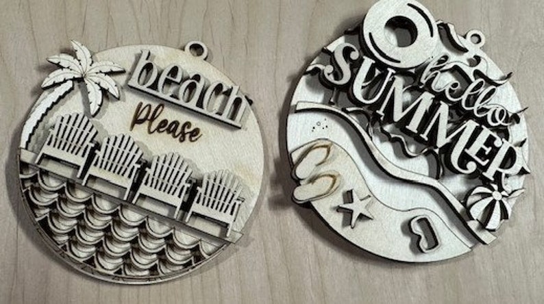 May include: Two round wooden ornaments with a summer theme. One ornament features a palm tree, beach chairs, and waves with the text "beach please". The other ornament features the text "hello summer" with a beach umbrella, flip flops, and a wave.