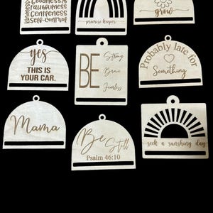 May include: Ten wooden ornaments with various sayings and designs. The ornaments are shaped like arches, rainbows, and sunbursts. Some of the sayings include "Love Joy Patience", "Be Strong Brave Fearless", "Yes This Is Your Car", "Mama", "Be Still Psalm 46:10", "Probably Late For Something", "Grow", "Seek A Sunshiny Day", and "Promise Keeper".