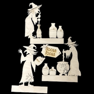 May include: A light-colored wooden cutout set featuring three witches, two shelves, four potion bottles, a cauldron, a spider, and a tag with the text Hocus Pocus. One witch holds a broom, another holds a book labeled Spells, and the third stirs a cauldron.