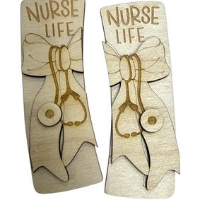 May include: Two wooden cutouts with the text "NURSE LIFE" above a bow and stethoscope design. The cutouts are light brown with darker brown detailing. The design is likely for a nurse or healthcare professional.