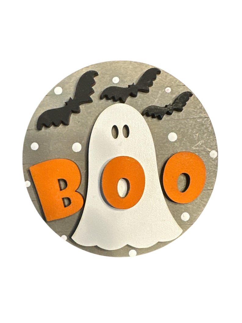 May include: A round wooden sign with a gray background and white polka dots. A white ghost with orange letters spelling "BOO" is in the center. Black bats are flying around the ghost.