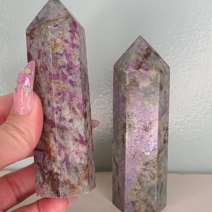 May include: Two purple and grey crystal points, one is larger than the other. The points are faceted and have a natural, rough texture.