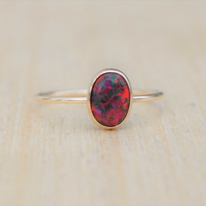 May include: A delicate gold ring with a red and black oval opal gemstone.
