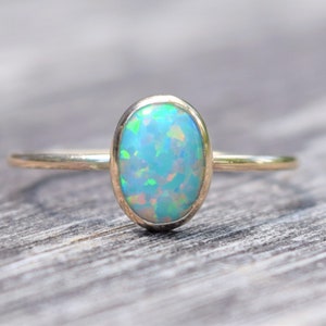 May include: A delicate gold ring with a light blue oval opal gemstone.