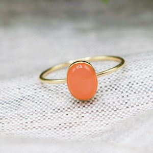 May include: A gold ring with a peach-colored oval gemstone.