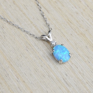 May include: A silver chain necklace with a blue opal pendant. The pendant is oval shaped and has a small diamond accent.
