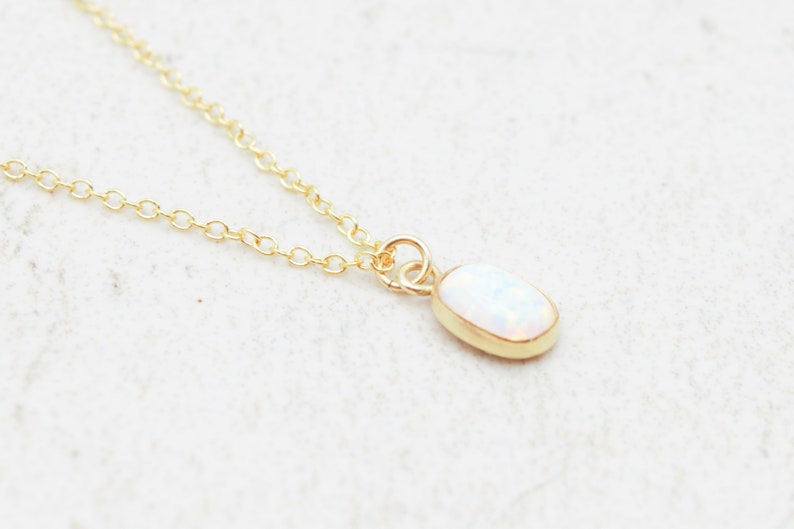 May include: A delicate gold chain necklace with a small oval opal pendant.
