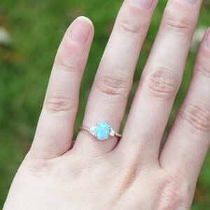 May include: A silver ring with a light blue oval opal gemstone and two smaller clear gemstones on the band.