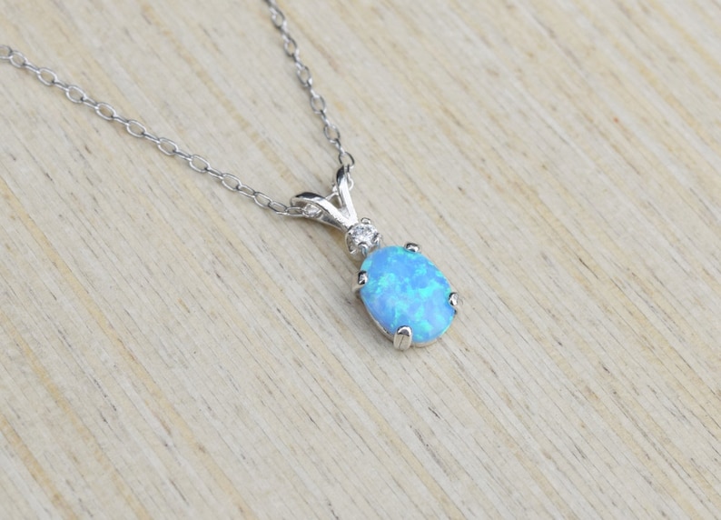 May include: A silver chain necklace with a blue opal pendant. The pendant is oval shaped and has a small diamond accent.