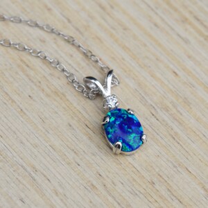 May include: A silver chain necklace with a blue opal pendant. The pendant is oval shaped and has a silver setting. The opal has a blue, green, and black color.