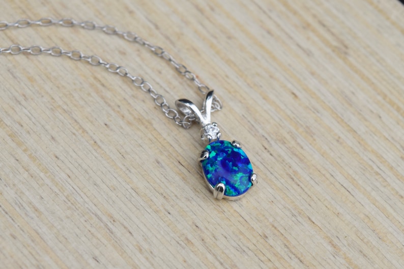 May include: A silver chain necklace with a blue opal pendant. The pendant is oval shaped and has a silver setting. The opal has a blue, green, and black color.