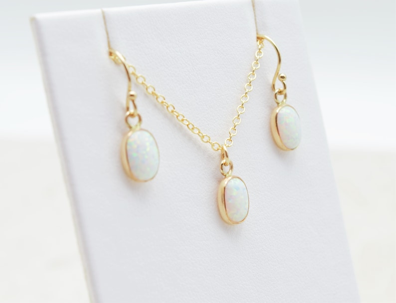May include: A gold chain necklace and matching earrings with oval-shaped white opal stones.