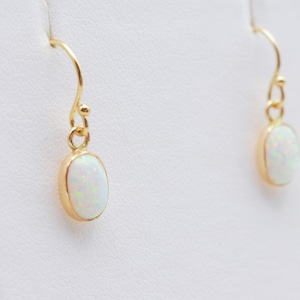 May include: A pair of gold earrings with oval-shaped white opal stones.