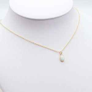 May include: A delicate gold chain necklace with a small oval-shaped white opal pendant.