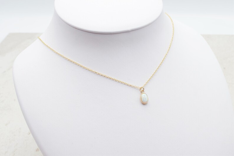 May include: A delicate gold chain necklace with a small oval-shaped white opal pendant.