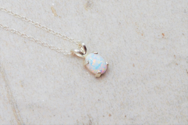 Puede incluir: Un collar de cadena de plata con un colgante de &oacute;palo blanco. El &oacute;palo tiene forma ovalada y est&aacute; engastado en un delicado marco de plata.