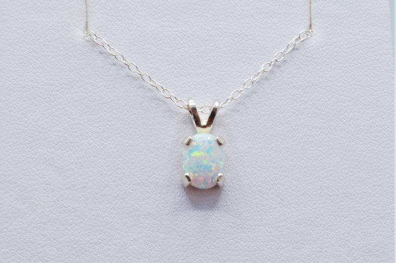 Puede incluir: Un collar de cadena de plata con un colgante de &oacute;palo blanco. El &oacute;palo tiene forma ovalada y tiene un delicado engaste de plata.