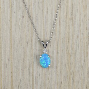 May include: A silver chain necklace with a blue opal pendant. The pendant is oval shaped and has a small diamond accent.