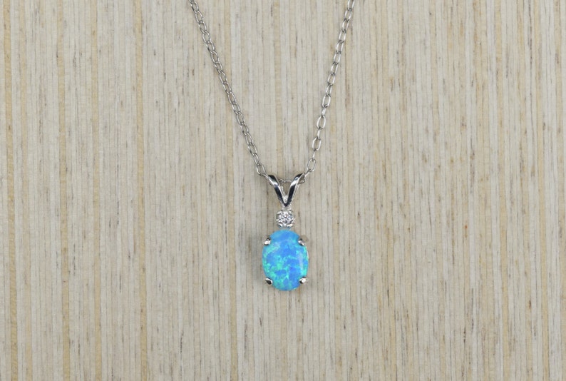 May include: A silver chain necklace with a blue opal pendant. The pendant is oval shaped and has a small diamond accent.